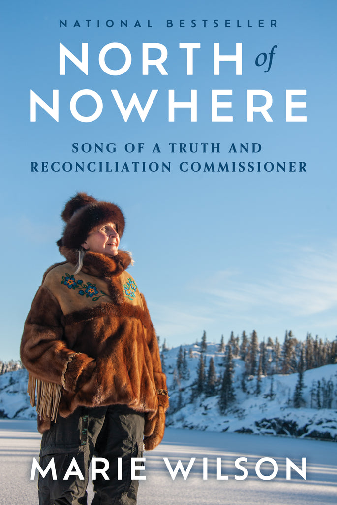  Cover: North of Nowhere, Song of a Truth and Reconciliation Commissioner by Marie Wilson. Marie Wilson stands in a flat, snowy field against a backdrop of snow-dusted hills with coniferous trees under a blue sky with a wisp of cloud. Marie Wilson smiles and looks to the side into the sun. She wears grey pants, a fur hat, and a parka with fringed sleeves and blue and orange beaded flowers. One hand is in her parka pocket, and the other hangs by her side wearing a mitten. 