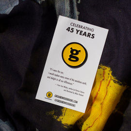  Photo: A circular enamel pin emblazoned with the Groundwood Books logo. The pin is attached to a white rectangular card which reads 