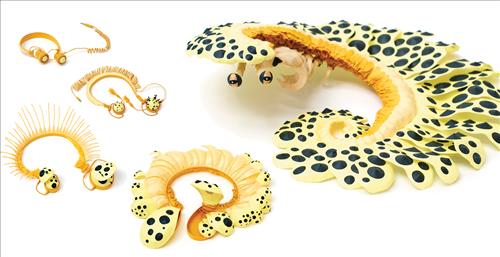  Through a series of five photographic scenes, a pair of orange headphones with a spiral wire transform into a yellow centipede with black dots. The centipede is made of paper materials. 