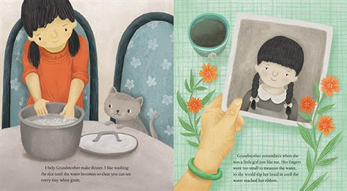  This image is a double page spread. To the left is a girl with medium skin tone and a cat at a table with a pot of water. The text says she helps her grandmother by washing the rice for dinner. To the right, a hand with medium skin tone has a black and white photo of a girl with medium skin tone with two braids and bangs. The text says her grandmother remembers when she was a little girl. Her fingers were too small to measure the water, so she would dip her braid in until the water reached her ribbon. 